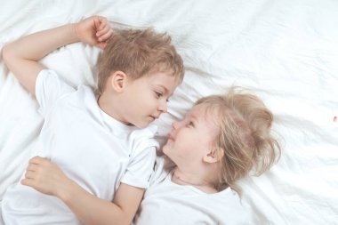 Beyaz tişörtlü çocuklar yatağa uzanıyorlar. kız ve erkek kardeş birlikte.