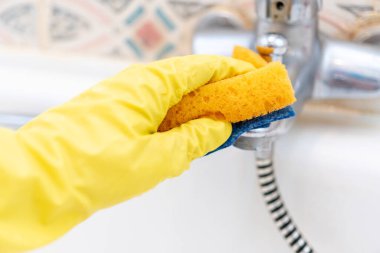 Banyoyu temizliyorum. Ev halkı. Sarı lastik eldiven. Krom banyo armatürlerini temizlemek