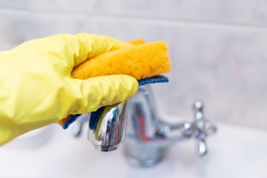 Banyoyu temizliyorum. Ev halkı. Sarı lastik eldiven. Krom banyo armatürlerini temizlemek