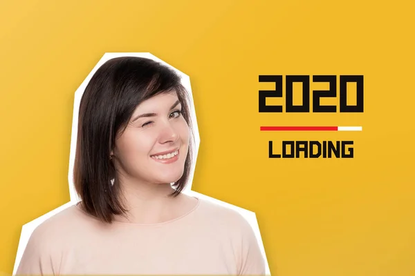 The brunette blinks her eye and smiles . Text download 2020 on yellow background. Waiting for the new year 2021