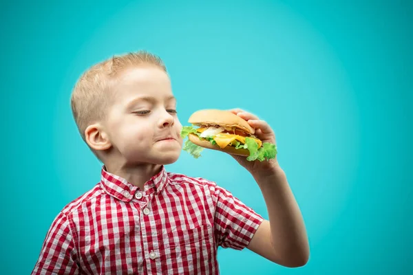 boy eats a Burger. kids love hamburger. the boy in the red shirt on a blue background