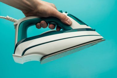 Bir adamın eli mavi arka planda bir ütü tutar. Bir erkek evde kadın işi yapar. Bir adam giysileri ütüler.