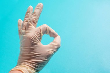 Tıbbi kauçuk eldiven mavi arka planda iyi bir jest olduğunu gösteriyor. Plastik eldivenli doktor eli.