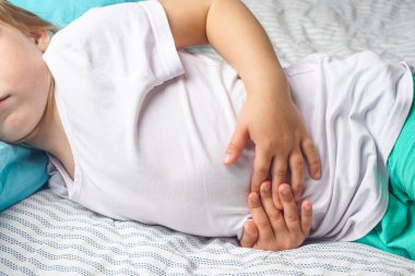 Anaokulundaki bir çocukta karın ağrısı. Çocuklarda zehirlenme. Çocuk ellerini karın boşluğuna dayamış.