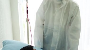 Doktor, hastane yatağında Coronavirus yüzünden öksüren hasta bir hastayla ilgileniyor. Hasta adam hastane yatağında yatıyor..