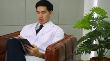 Doktor hastanede çalışırken stresli oluyor. Hastane ofisinde hasta sağlığı verileriyle çalışan bir doktor. Laboratuvar önlüklü ve gözlüklü profesyonel erkek doktor ofiste dizüstü bilgisayarla çalışıyor.