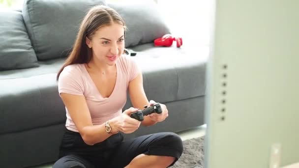 年轻的女性开玩笑地坐在家里的一个操场上玩电子游戏 呆在家里 男人手里拿着游戏机控制器玩 — 图库视频影像