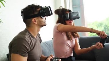 VR ya da sanal gerçeklik gözlüğü takan bir çift, evdeki kanepede oturup video oyunu oynayan teknoloji ve yenilik kavramı. Eğleniyorum. Eğlence konsepti.