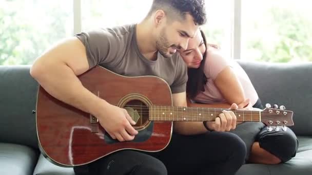 男人在客厅和妻子的女朋友一起弹奏吉他手 男人为情人唱情歌 欢欢喜喜的情侣在客厅里一起弹奏吉他 — 图库视频影像