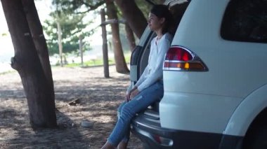 Gezgin araba konsepti. Yalnız ve mutlu genç bir kadın gezgin sahilde ve hatchback arabasında oturuyor..