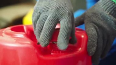 Gaz maskeli bir adam kırmızı galonda yağ kontrolü yapıyor.