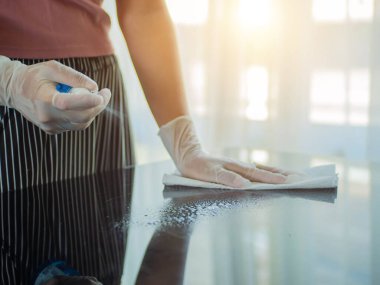 COVID-19 içeriyi sterilize ediyor. Ev masasını temizlemek mutfak masasının yüzeyini dezenfektan sprey şişesiyle temizlemek yüzeyi havlu ve eldivenle yıkamak..
