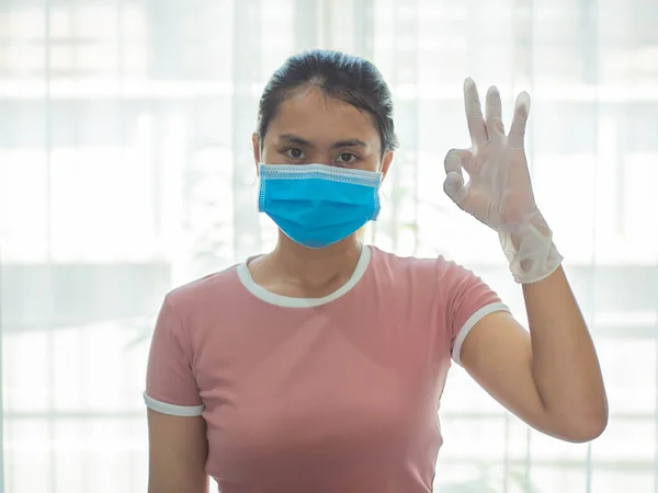 Corona virüsü için ameliyat maskesi takan bir kadın. Tıbbi maske takan genç bir kadın, stüdyo resmi. İnsanlar temizlik ve dezenfekte konsepti. Eldivenli ve koruyucu maskeli bir kadın işaret yapıyor..