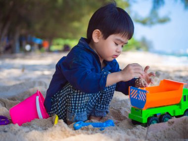 Tropik plajda oynayan bir çocuk. Aile yaz tatili. Kumsalda kum aletleriyle oynayan sevimli küçük çocuk..