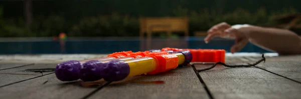 Havuz başında oyuncak su tabancası ve bir çocuğun eli.