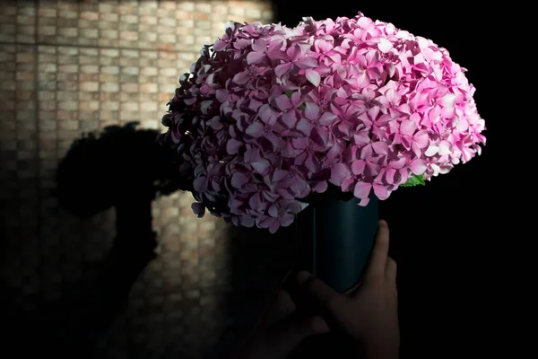 Yeşil vazo, duvarda yansıması ve pembe çiçekleri olan küçük çocuğun ellerinde.