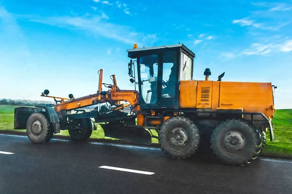 Road scraper on the asphalt against the background of a green meadow and blue sky