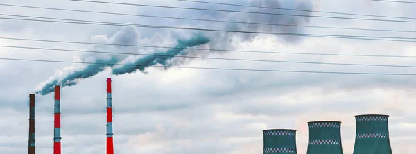 Environmental pollution, environmental problems, smoke from the pipes and cooling tower of an industrial enterprise or a thermal power plant against a dark grey sky background