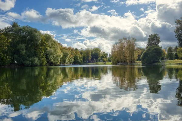 Güneşli bir günde güzel bulutları olan mavi gökyüzüne karşı gölün sularındaki ağaçların yansıması..