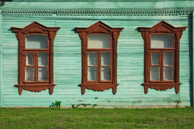 Ahşap oyma ile dekore edilmiş eski bir Rus evinin duvarında arka arkaya üç pencere.