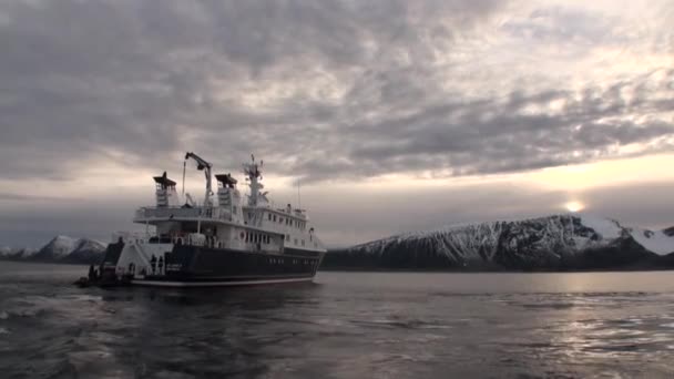 Menschen im Boot schwimmen zu großen Jachten und Schneehöhen des Berges und grauen Himmels in der Arktis. — Stockvideo