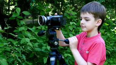 Genç oğlan video kameraya yeşil park arka plan üzerinde görünüyor..