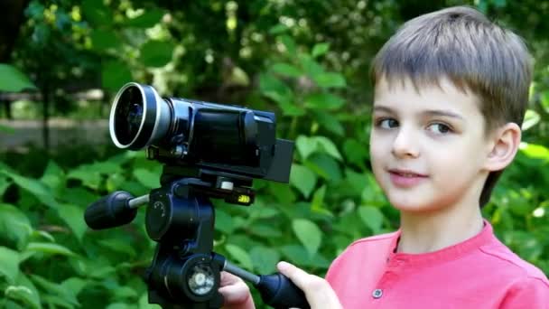 Kleiner Junge blickt in Videokamera im Hintergrund des grünen Parks. — Stockvideo