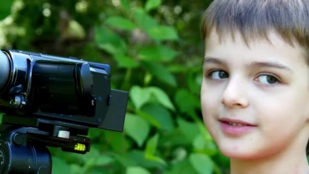 Jeune garçon regarde dans la caméra vidéo sur fond de parc vert . — Video