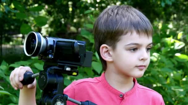 Kleiner Junge blickt in Videokamera im Hintergrund des grünen Parks. — Stockvideo