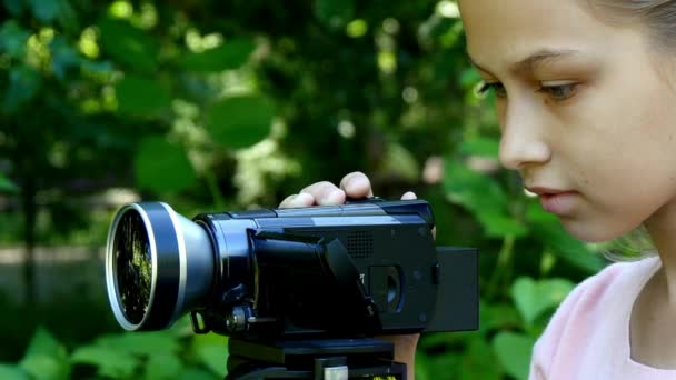 Menina olha para a câmera de vídeo no fundo do fundo do parque verde . — Vídeo de Stock
