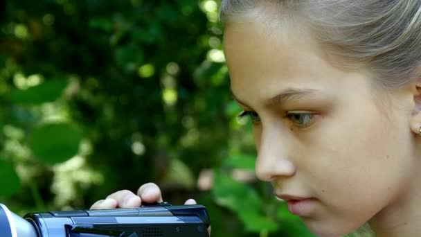 Ung flicka ser in videokamera på bakgrund av grön park bakgrund. — Stockvideo