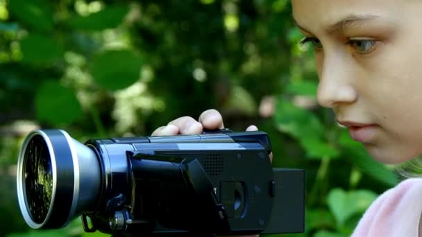 Jong meisje kijkt naar videocamera op achtergrond van groene park achtergrond. — Stockvideo