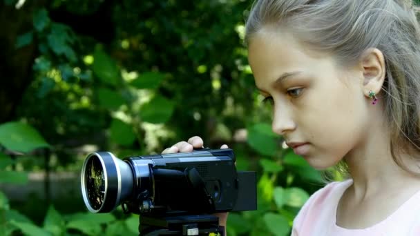 Menina olha para a câmera de vídeo no fundo do fundo do parque verde . — Vídeo de Stock