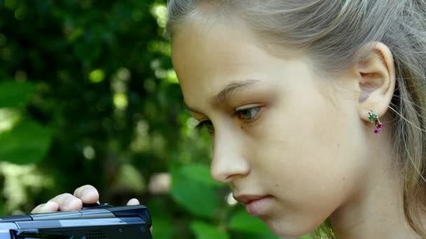 Молода дівчина дивиться у відеокамеру на фоні зеленого парку . — стокове відео