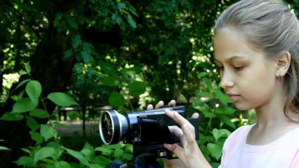 Menina olha para a câmera de vídeo no fundo do fundo do parque verde . — Vídeo de Stock