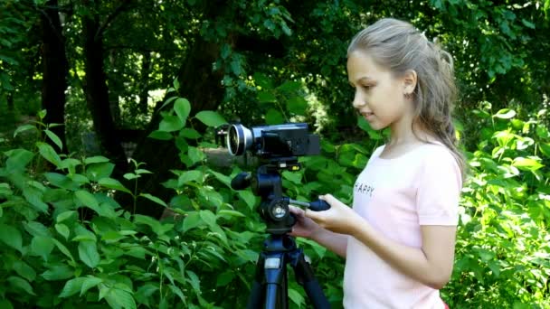 若い女の子は、緑豊かな公園の背景の背景にビデオ カメラに見える. — ストック動画