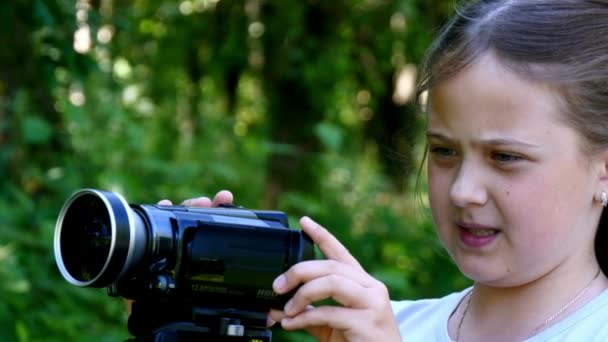 Fiatal lány úgy néz ki, a videó kamera a háttér-háttér zöld park. — Stock videók