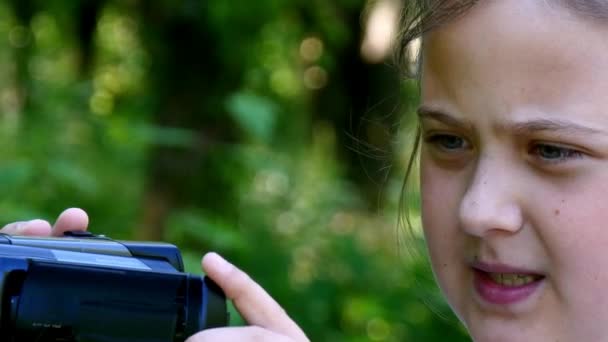 Młoda dziewczyna wygląda na kamery wideo na tle zielonego parku tła. — Wideo stockowe