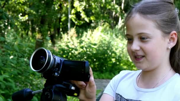 Menina olha para a câmera de vídeo no fundo do fundo do parque verde . — Vídeo de Stock