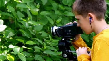 Genç çocuk video kamera ile film yeşil park arka plan doğası hakkında vuruyor.