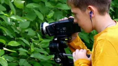 Genç çocuk video kamera ile film yeşil park arka plan doğası hakkında vuruyor.