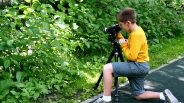 Genç çocuk video kamera ile film yeşil park arka plan doğası hakkında vuruyor.