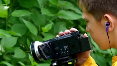 Genç çocuk video kamera ile film yeşil park arka plan doğası hakkında vuruyor.