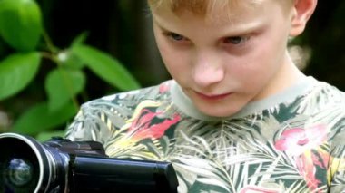 Genç çocuk video kamera ile film yeşil park arka plan doğası hakkında vuruyor.
