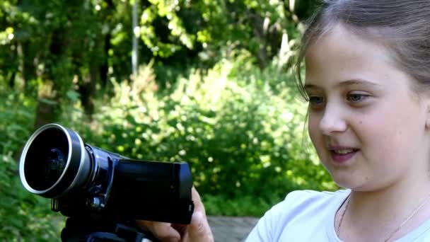 Jong meisje kijkt naar videocamera op achtergrond van groene park achtergrond. — Stockvideo