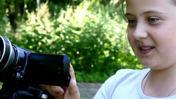 Молода дівчина дивиться у відеокамеру на фоні зеленого парку . — стокове відео