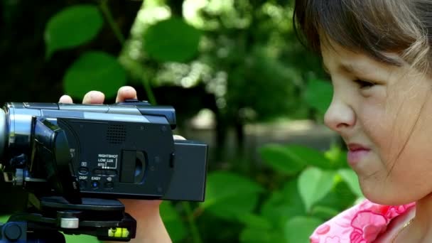 Mladá dívka vypadá na video kameru na pozadí pozadí zelený park. — Stock video