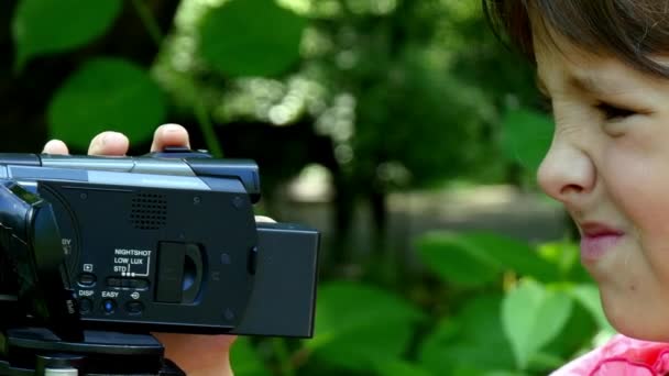 Jeune fille regarde dans la caméra vidéo sur fond de fond de parc vert . — Video