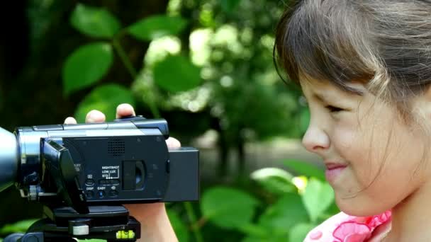 Ung flicka ser in videokamera på bakgrund av grön park bakgrund. — Stockvideo