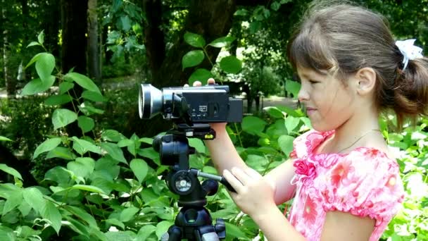 若い女の子は、緑豊かな公園の背景の背景にビデオ カメラに見える. — ストック動画